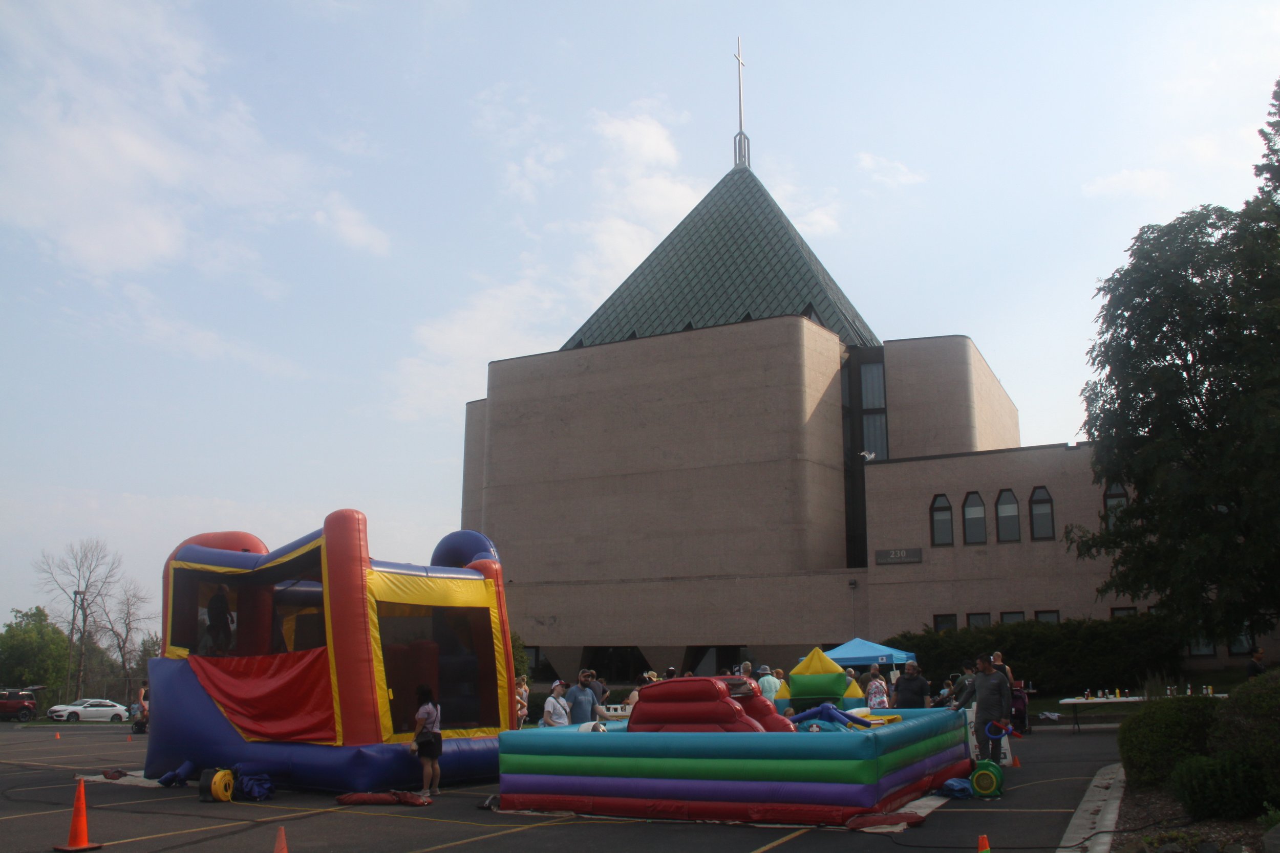 Inflatable bounce house and obstacle course set up in a parking lot outside a First United Methodist, with several children and adults nearby, under a partly cloudy sky.