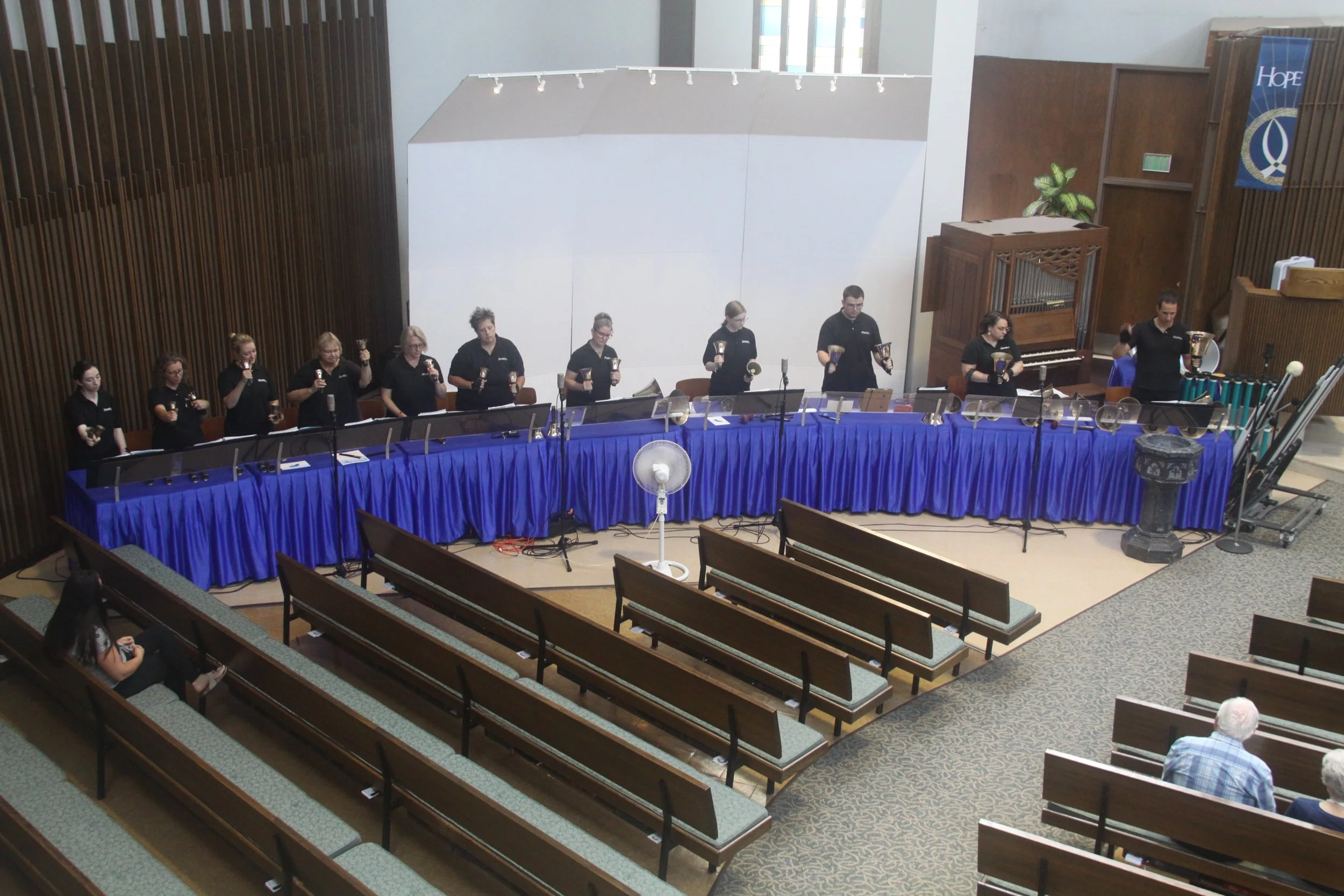 Strikepoint, First United Methodist's handbell group, performing, with people seated in the pews and a blue altar cloth.