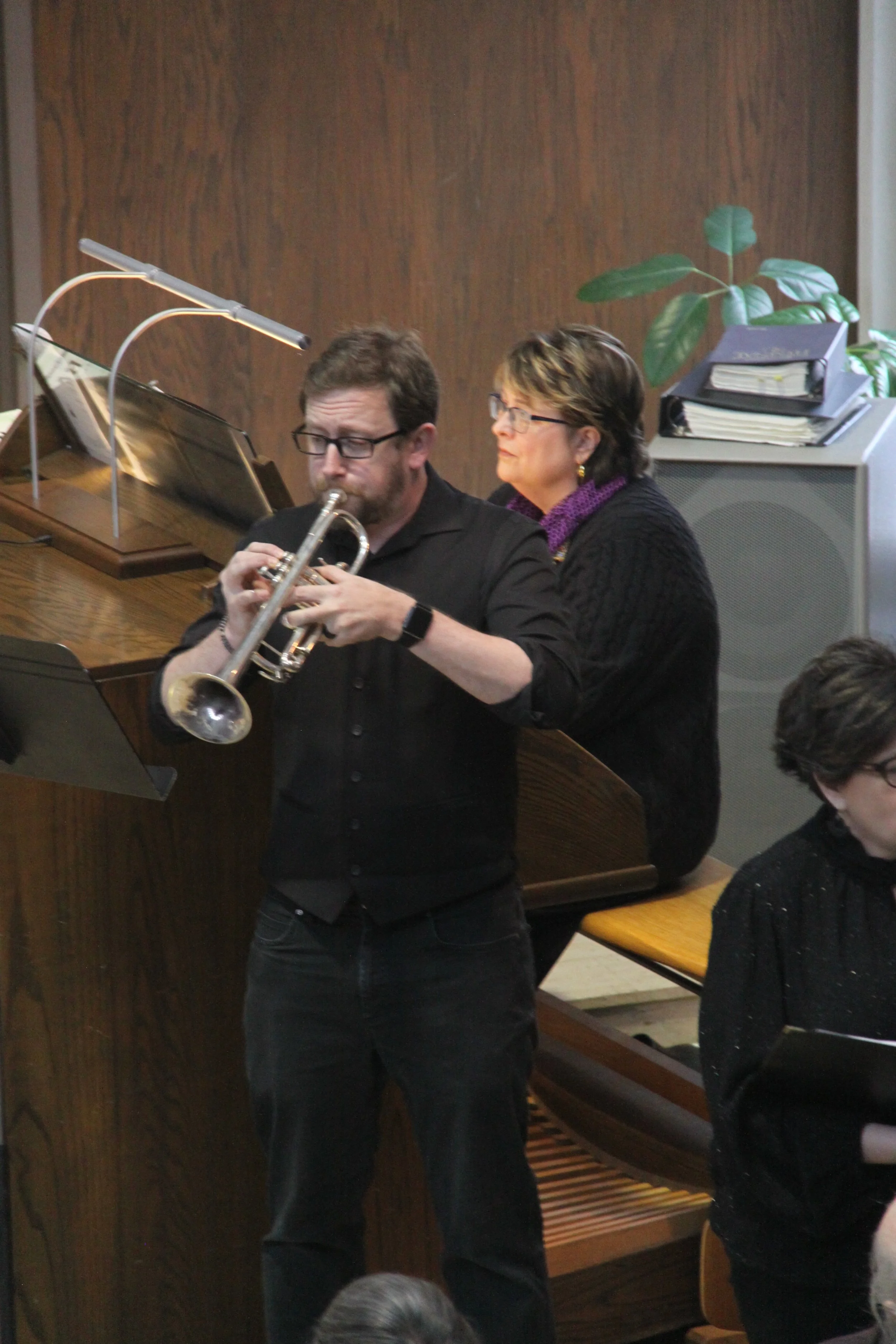 A man playing a trumpet while a woman accompanies him on a piano.