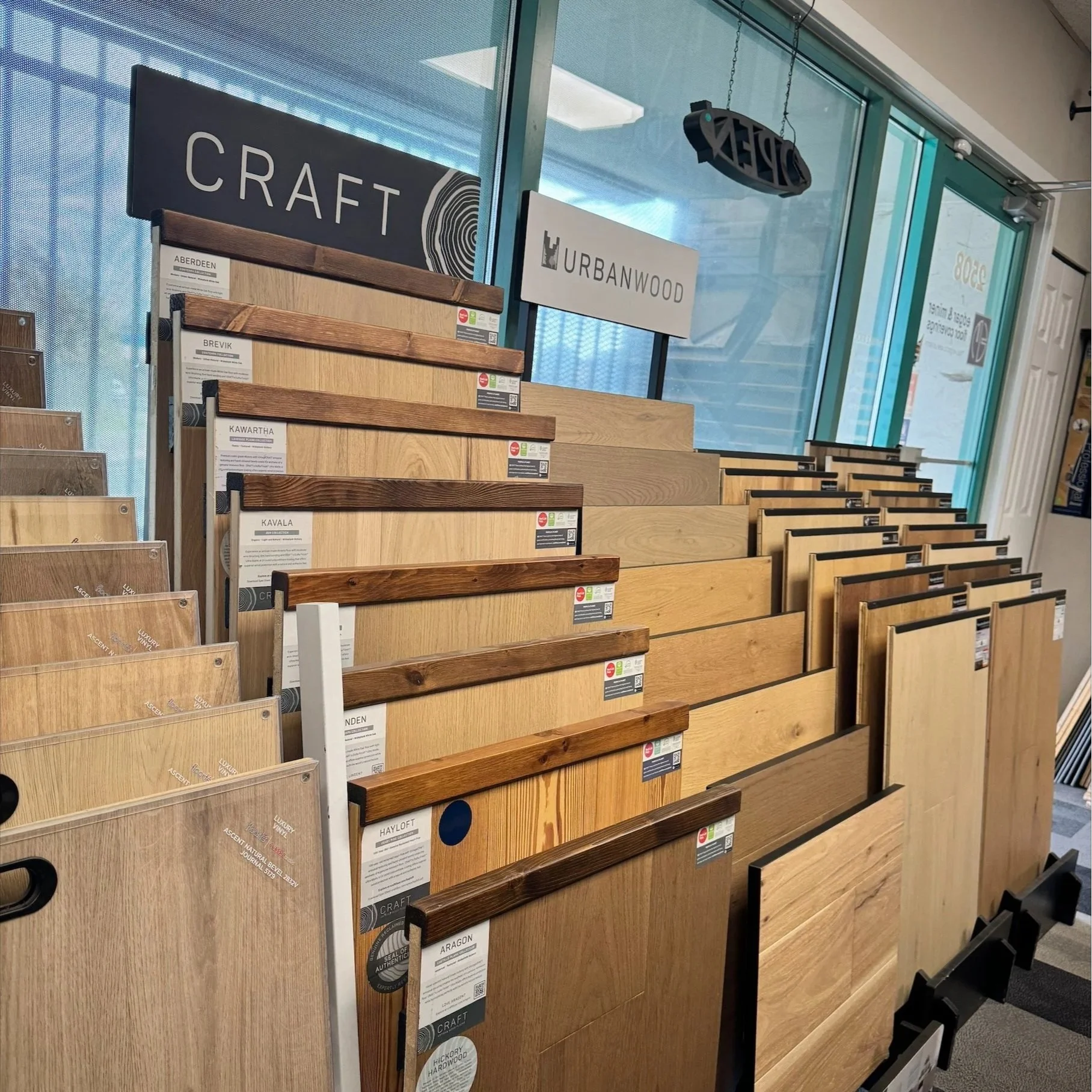 Display of various wood flooring samples in a store, labeled with brand names like 'Craft' and 'Urbanwood'.