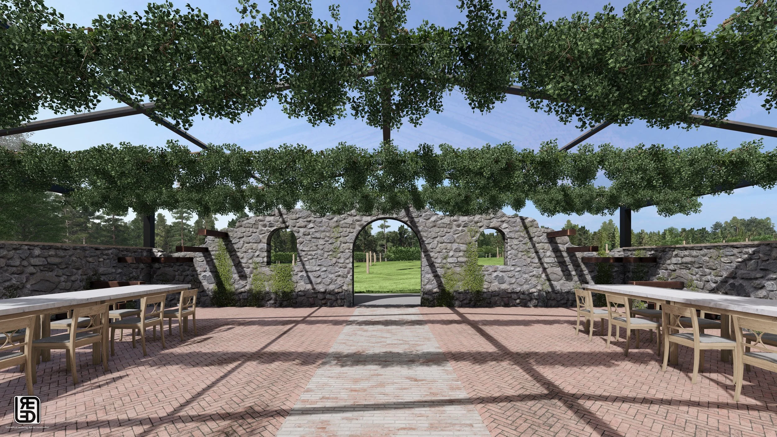 A covered outdoor stone patio with stone flooring, wooden tables and chairs, a stone archway, and lush greenery in the background.