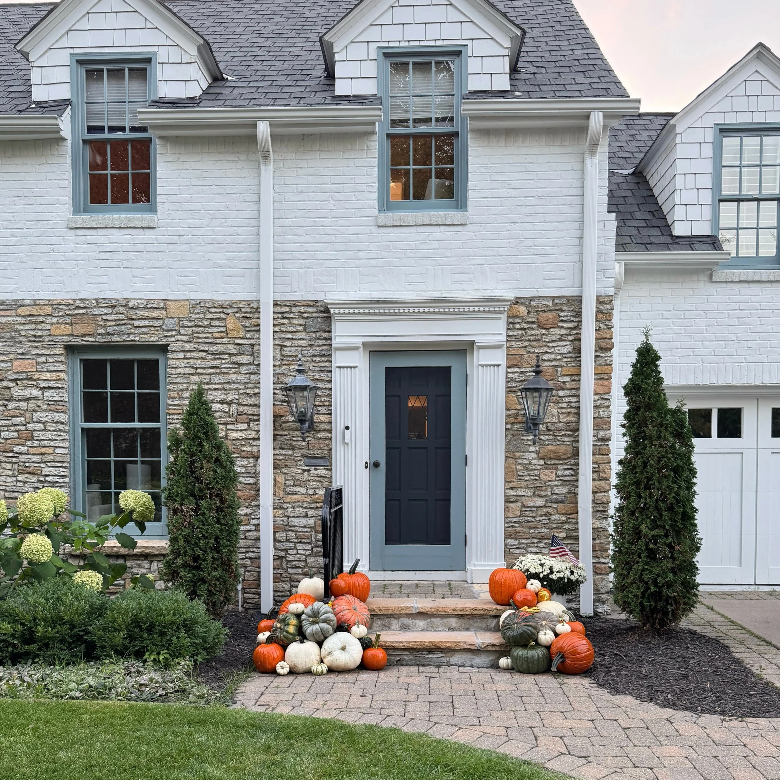 Front porch decorated with pumpkins and gourds, potted plants, and a wreath on the door for fall or Halloween.