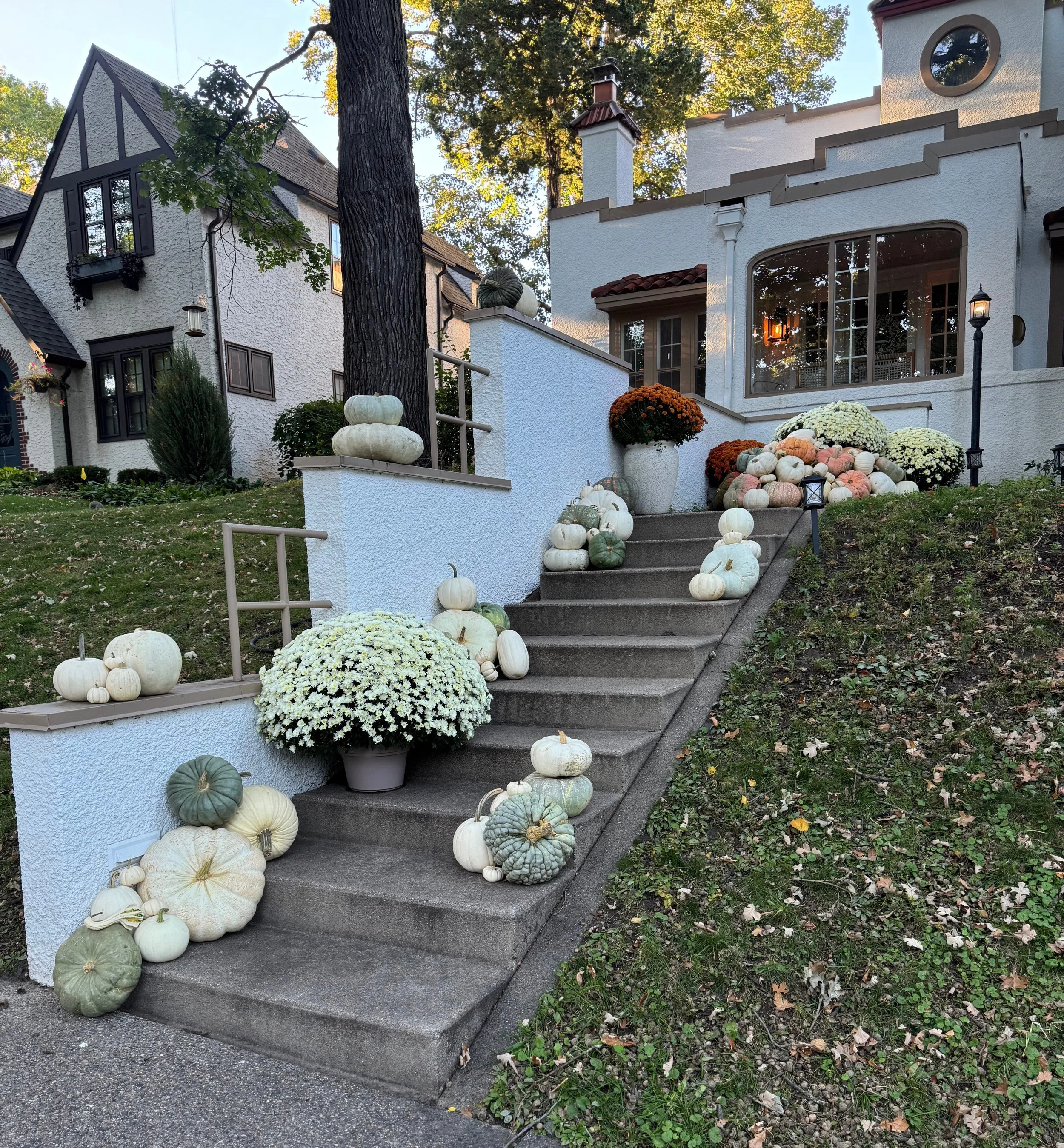 Front porch decorated with a variety of colorful pumpkins and gourds, a glass door with two wreaths hanging on it, and a lantern on the right side of the steps.