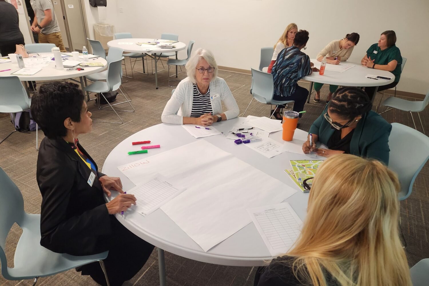 Women sitting around tables with papers and pens in a meeting or workshop setting.