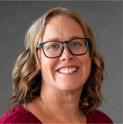 Close-up portrait of a smiling woman with glasses and wavy blonde hair, wearing a red top.
