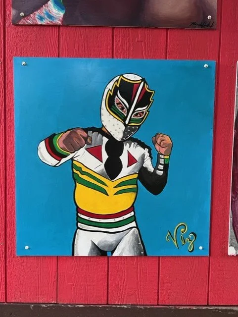 Colorful mural of a person in a luchador mask and wrestling costume, supporting their fists in a fighting stance, painted on a blue background.