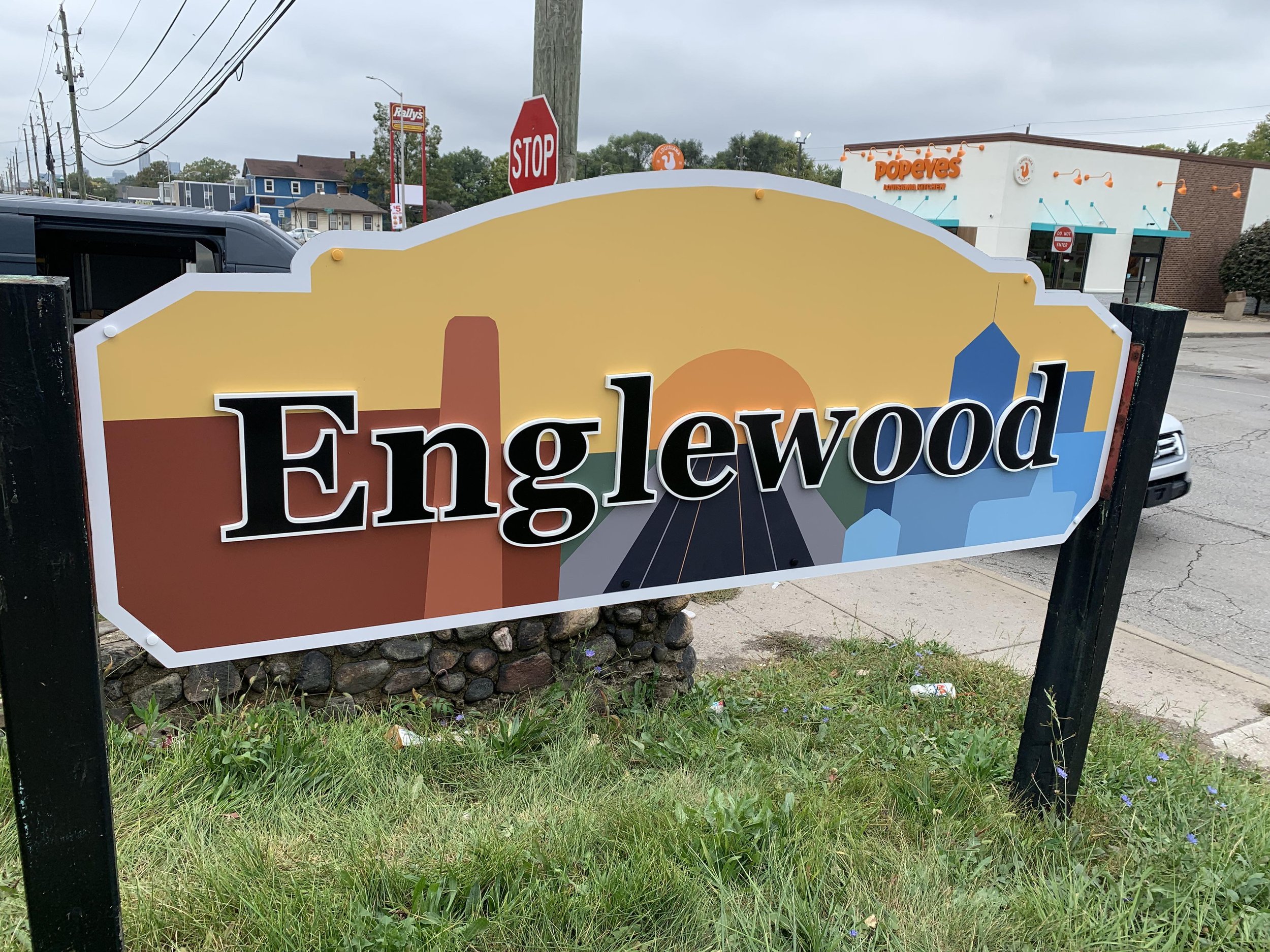 Sign for Englewood with a stylized sunset, buildings, and road in background.