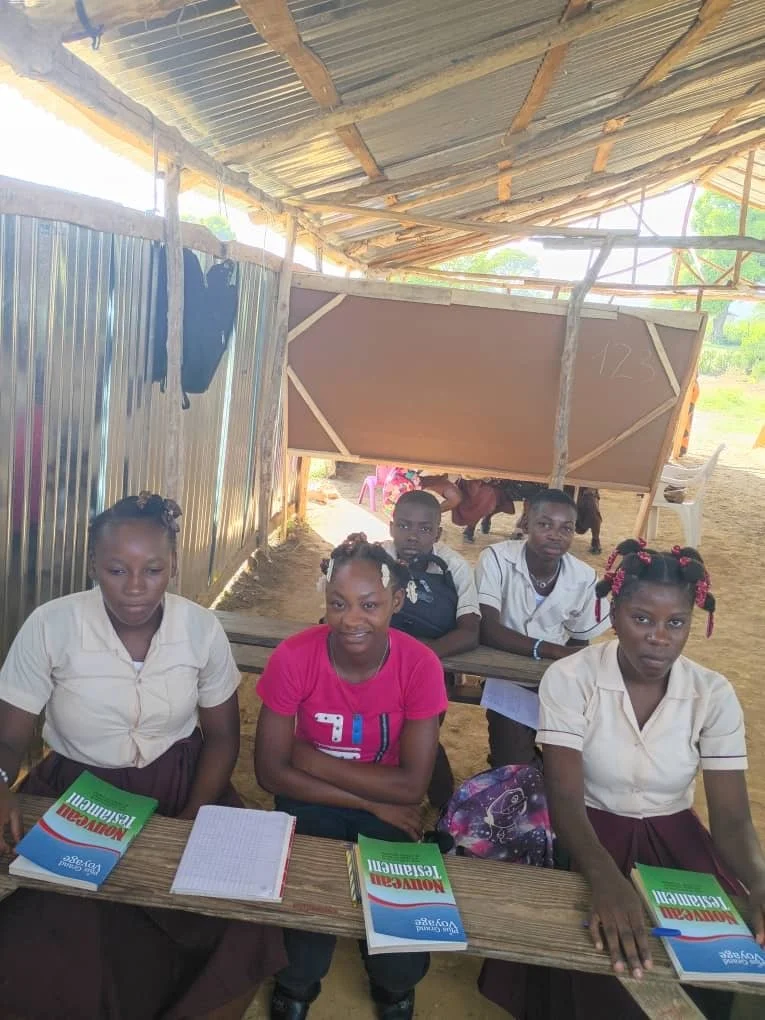 Students seated at wooden classroom desks with books and notebooks.