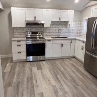 Modern kitchen with white cabinets, stainless steel appliances including a refrigerator and stove, gray subway tile backsplash, and wood-look flooring.