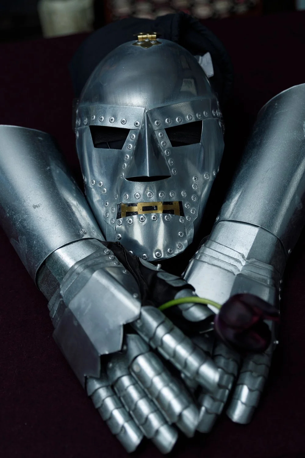 A metallic robot or costume with a skull-like mask, large shoulder armor, and detailed arm pieces lying on a dark surface.