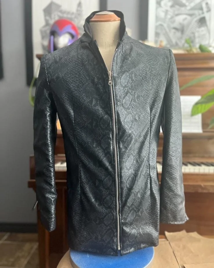 Black textured leather jacket with a zipper front, displayed on a mannequin in front of a piano.