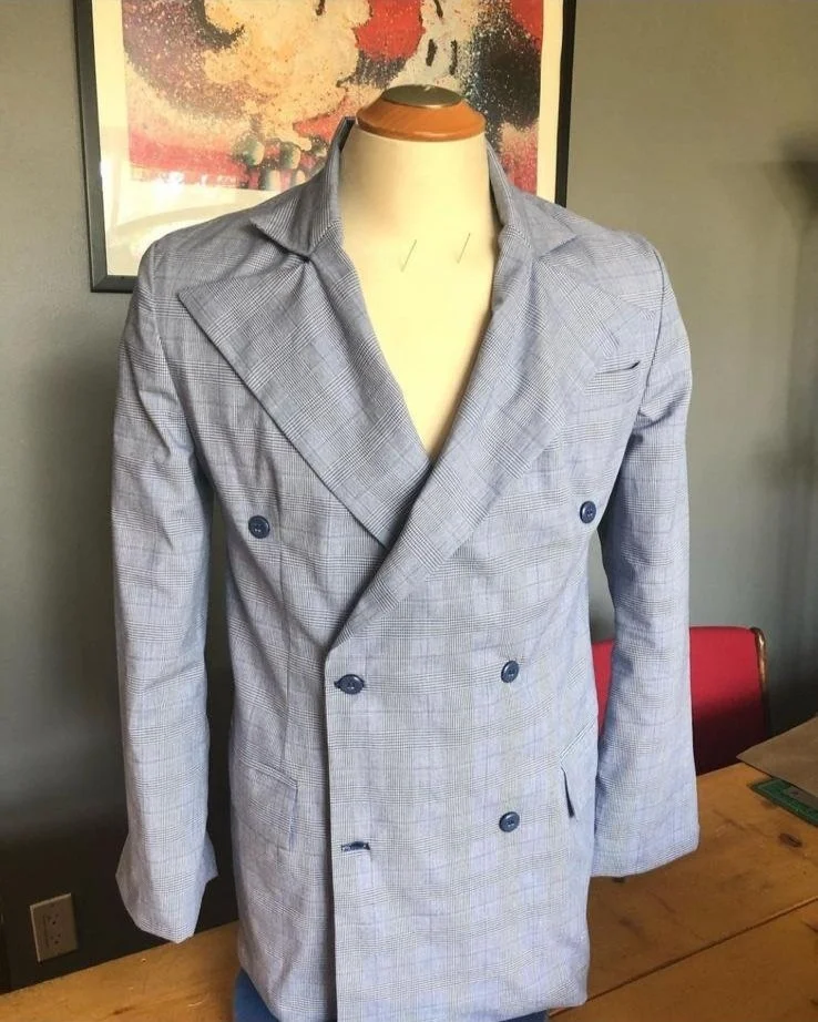 Gray double-breasted blazer with plaid pattern on a mannequin in front of a colorful abstract painting.