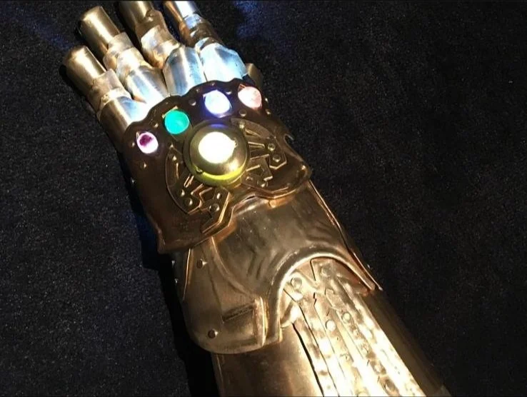 A robotic glove resembling Iron Man's gauntlet, with illuminated colored stones and a glowing centerpiece.