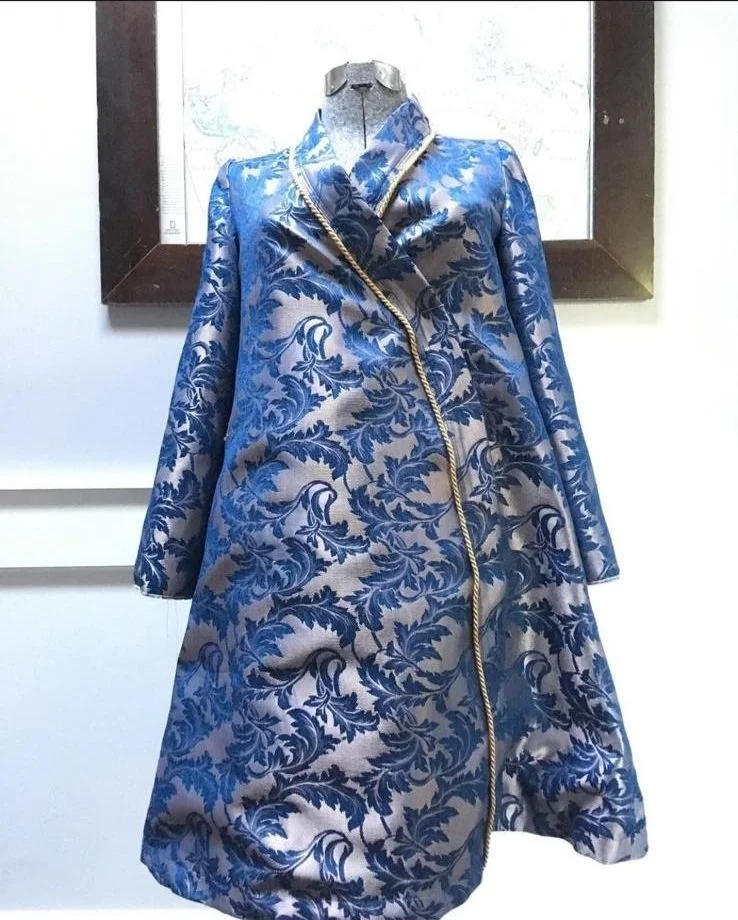 A blue and silver floral patterned coat displayed on a mannequin, with a high collar and gold trim along the zipper.