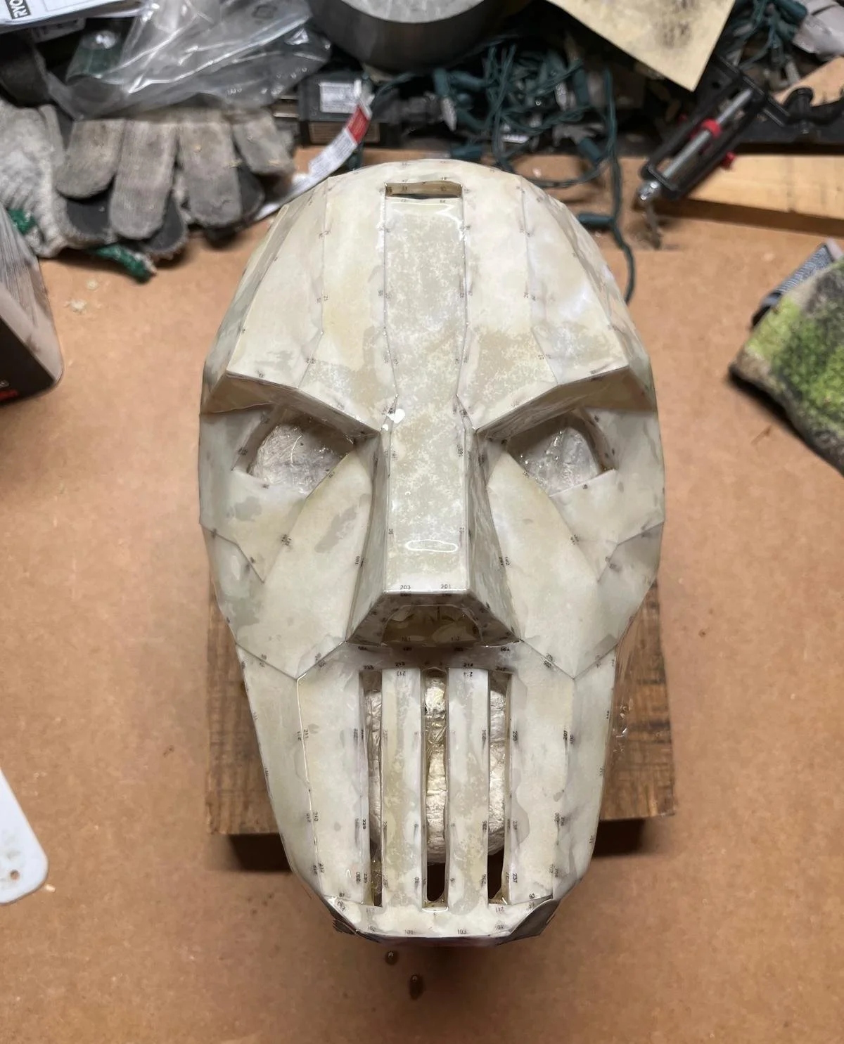 A work in progress, half-assembled skull mask with a geometric, angular design, on a workbench in a workshop.
