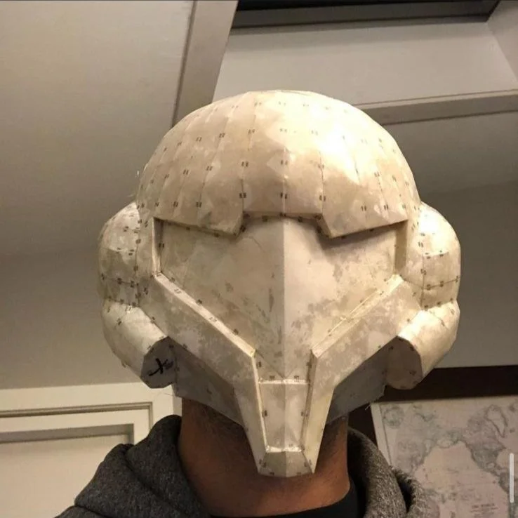 Person wearing a helmet that resembles Metroid, or a TIE Fighter from Star Wars, made of a light-colored material with visible construction details.