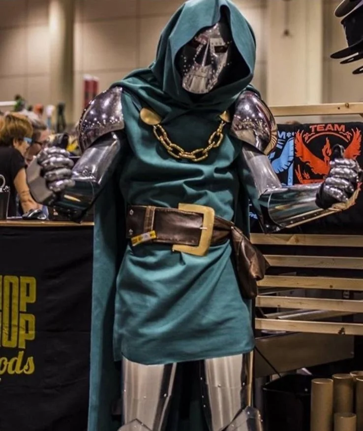 A futuristic robot dressed as a medieval fantasy character with armor, a cape, chain necklace, and belt, displayed at a convention.