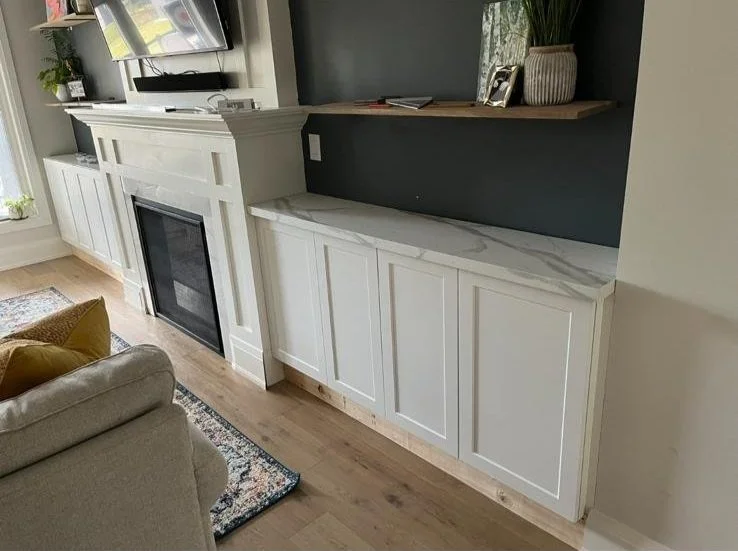 Living room with white built-in cabinet and marble countertop below a mounted TV, decorated with green plants and framed pictures.