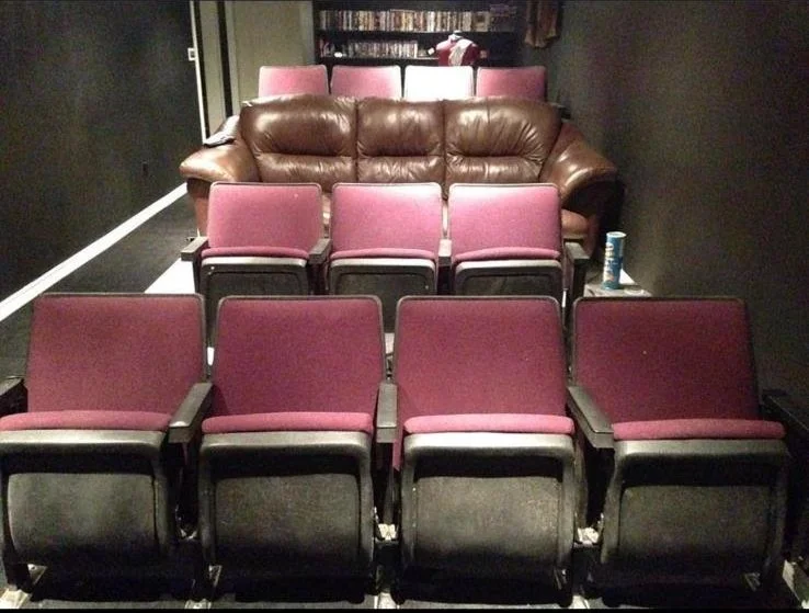A small theater room with eleven maroon theater seats arranged in three rows, with a brown leather couch at the back of the room.