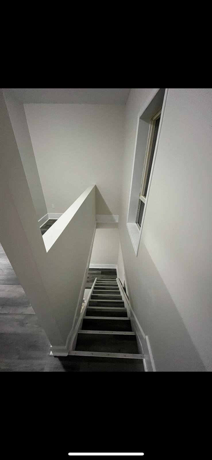 Interior view of a staircase with dark wood steps, white walls, and a window on the side, taken from a top vantage point.