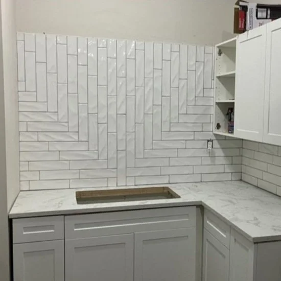 Kitchen corner with white tiled backsplash and white cabinets; sink area empty with open cabinet shelves.