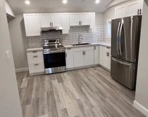 Modern kitchen with white cabinets, stainless steel refrigerator and stove, gray tiled backsplash, and wood-look flooring.