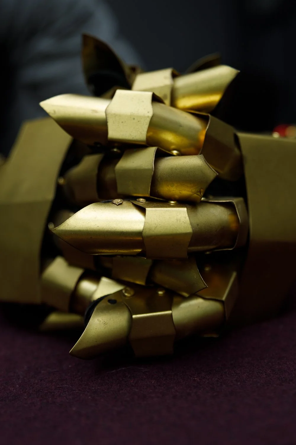 Close-up of a metallic object with interconnected, pointed, and rounded pieces in gold and bronze tones, resting on a dark surface.