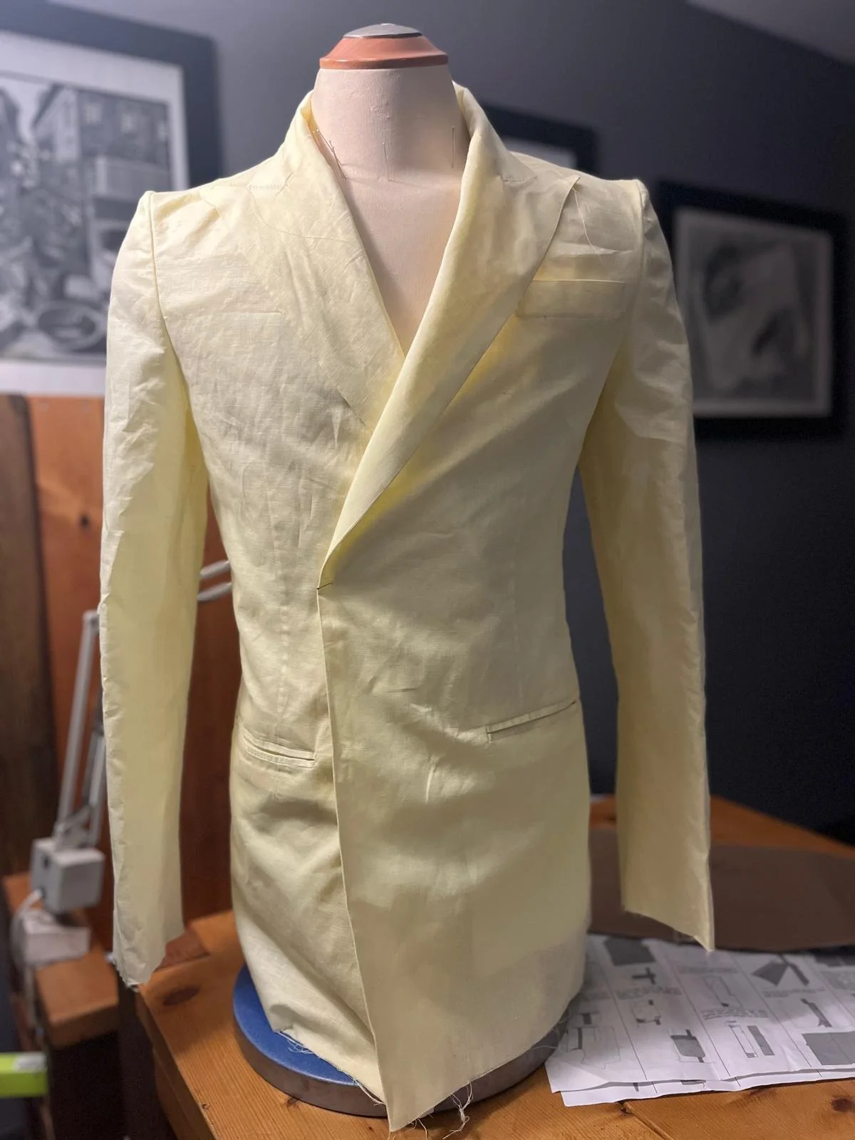 A yellow linen blazer displayed on a mannequin bust in a craft room, with papers and framed artwork in the background.