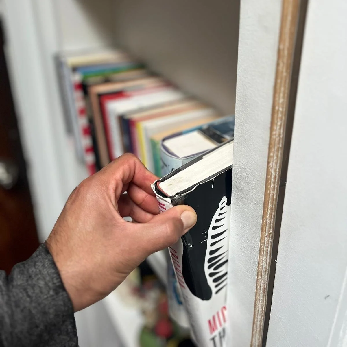 Person inserting a book into a wall-mounted paper holder on a bookshelf.