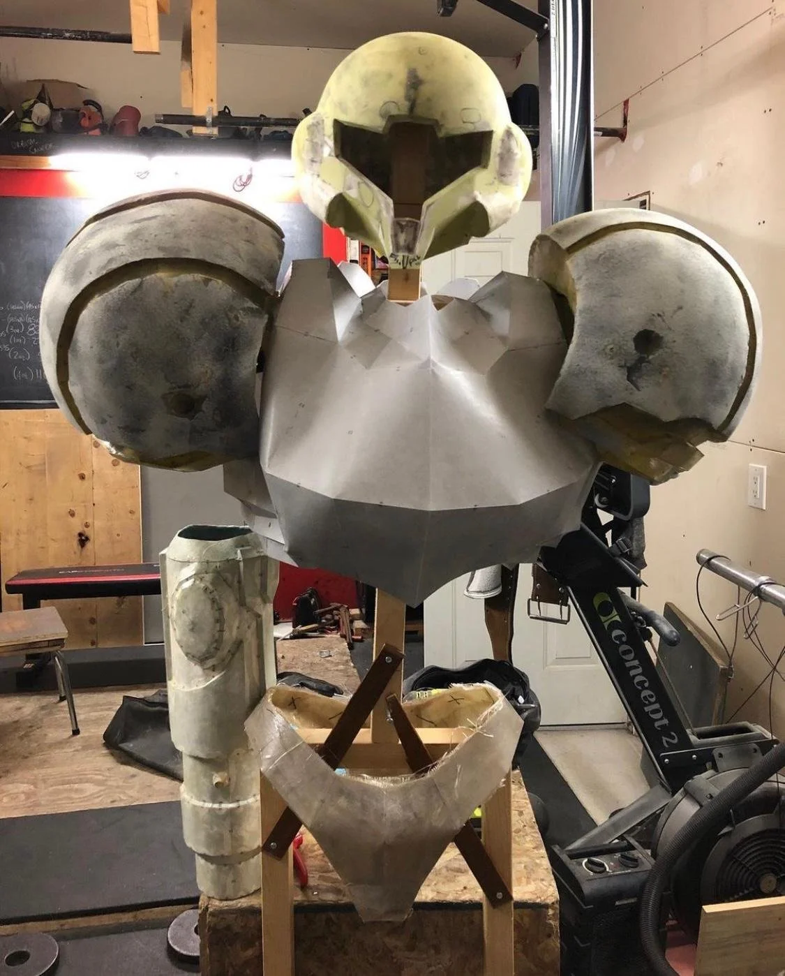 A work-in-progress model or costume of a robot with a stylized humanoid face, large shoulder pads, and chest armor in a workshop setting.