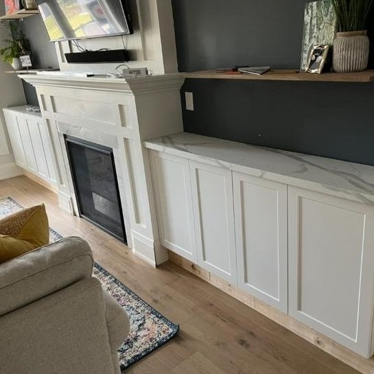 Living room with white built-in cabinets, a fireplace, a flat screen TV mounted on the wall, and a gray armchair with a yellow pillow.