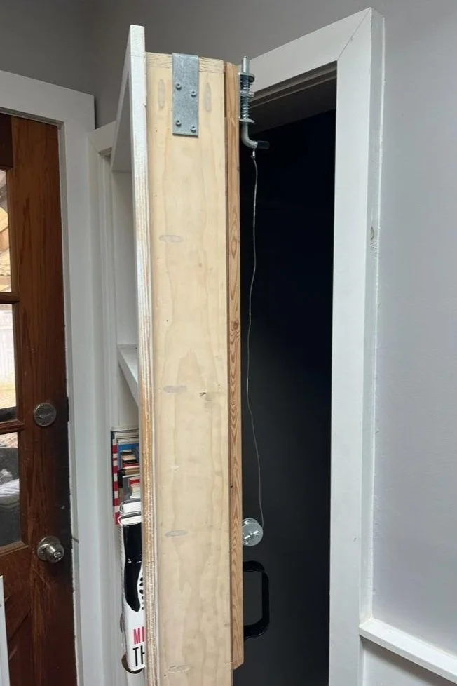 Partially constructed vertical wall frame with metal hardware, a hanging string, and a speaker in a room.