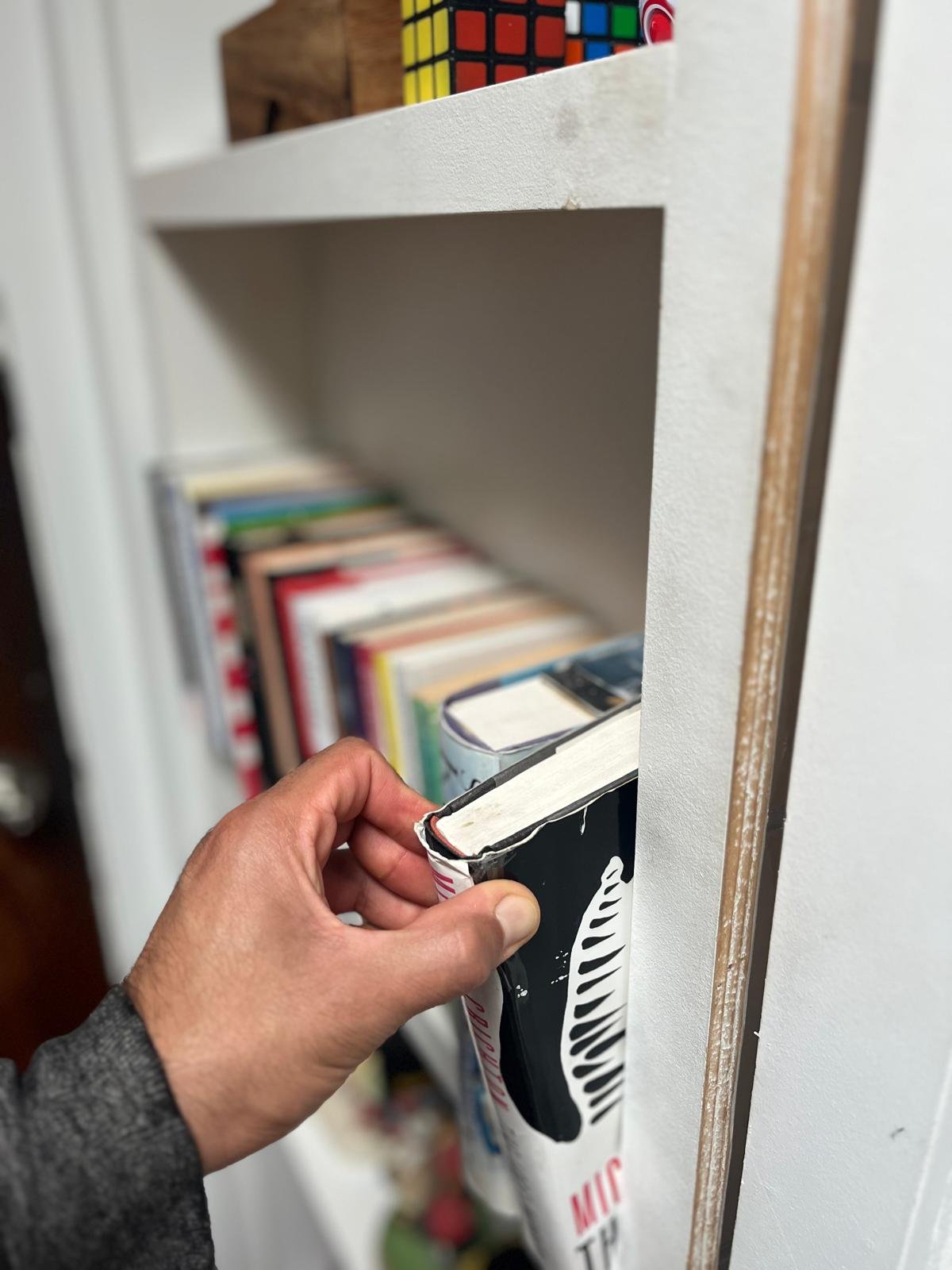 A person’s hand holding a the key to a secret door against a white bookshelf with books and a Rubik’s cube in the background.