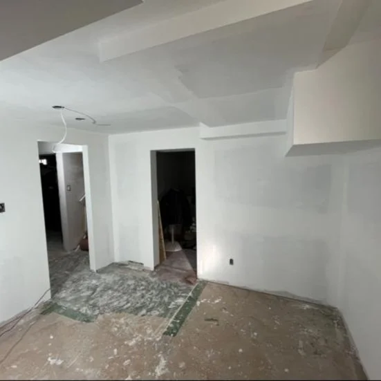 Interior of a room under construction or renovation with white walls, an unfinished floor, and an open doorway leading to another space.