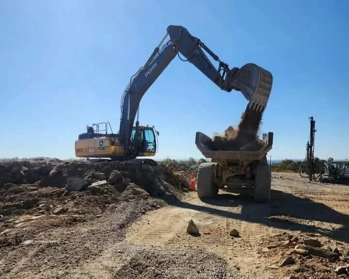 Excavator loading dirt and rocks into a dump truck at a construction site.