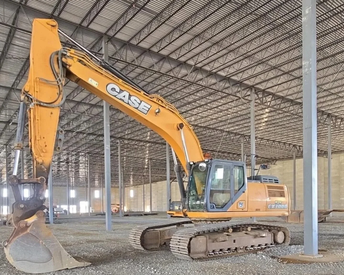 A large yellow case excavator inside a spacious warehouse with a metal roof and support beams.