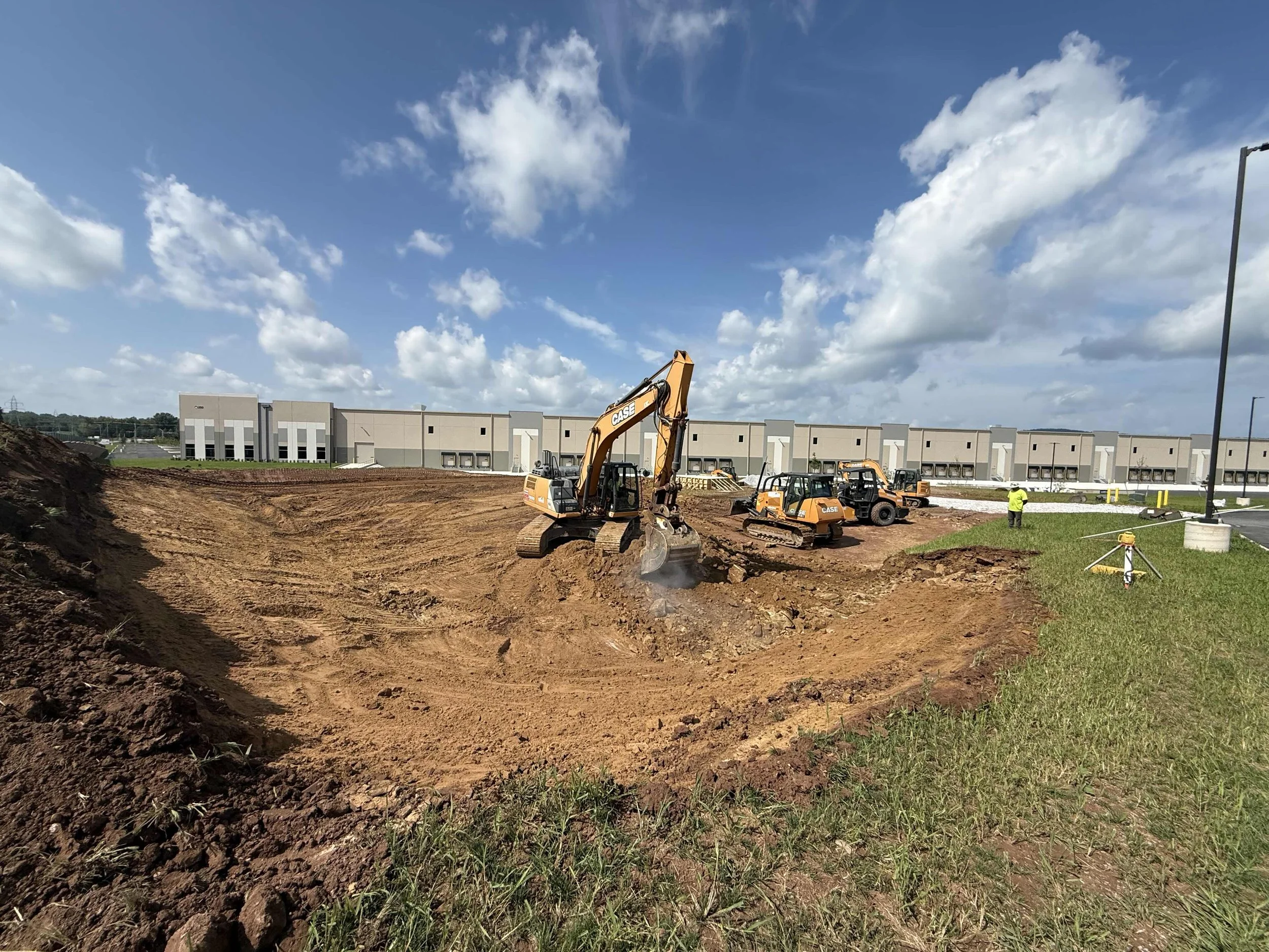 Construction site with excavator and workers, new building in background, on a partly cloudy day