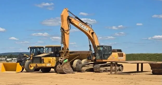 Construction site with heavy machinery, including an excavator and a bulldozer, working on a dirt road under a partly cloudy sky.
