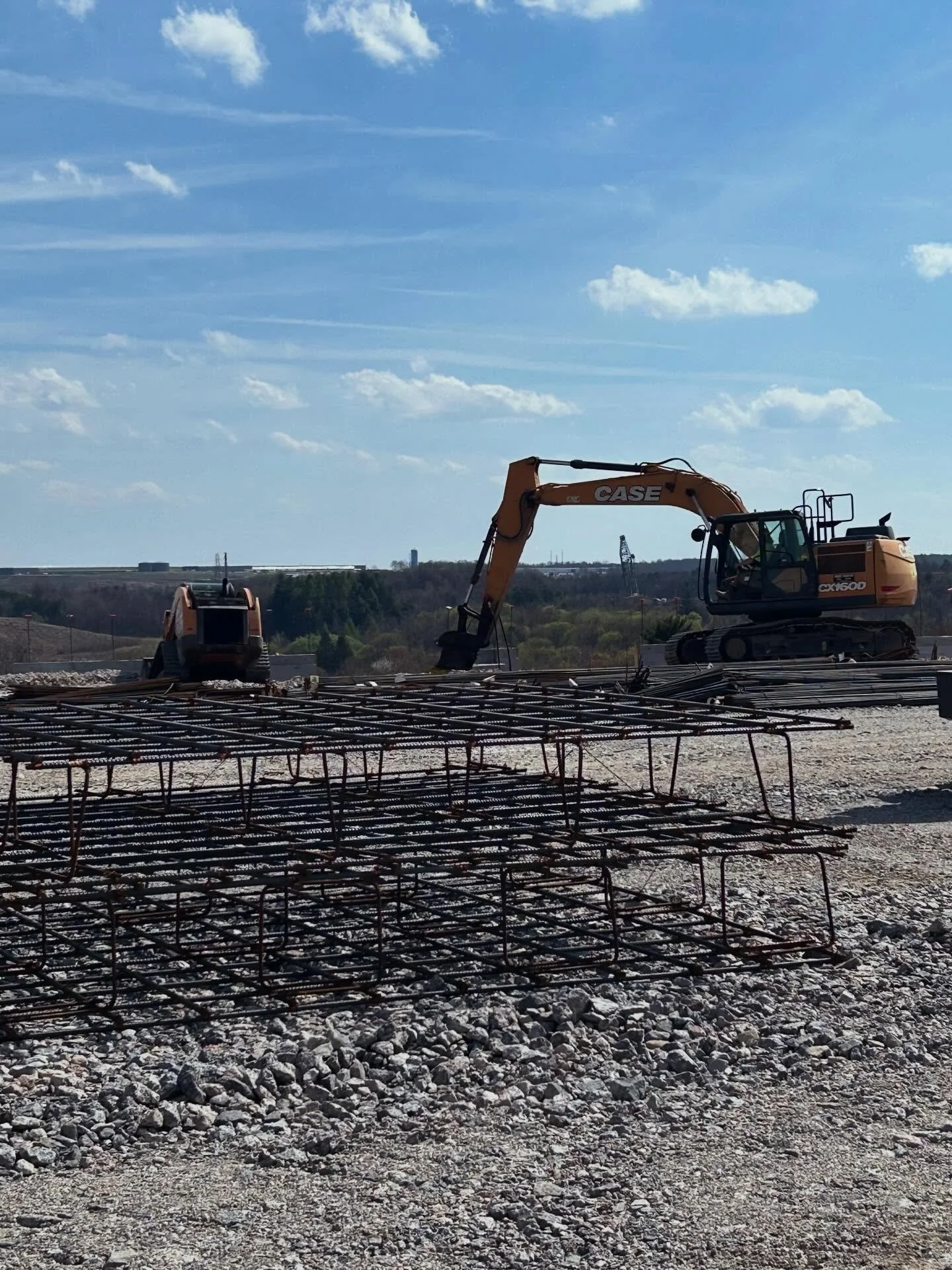 Construction site with rebar and a CASE excavator against a blue sky with scattered clouds.