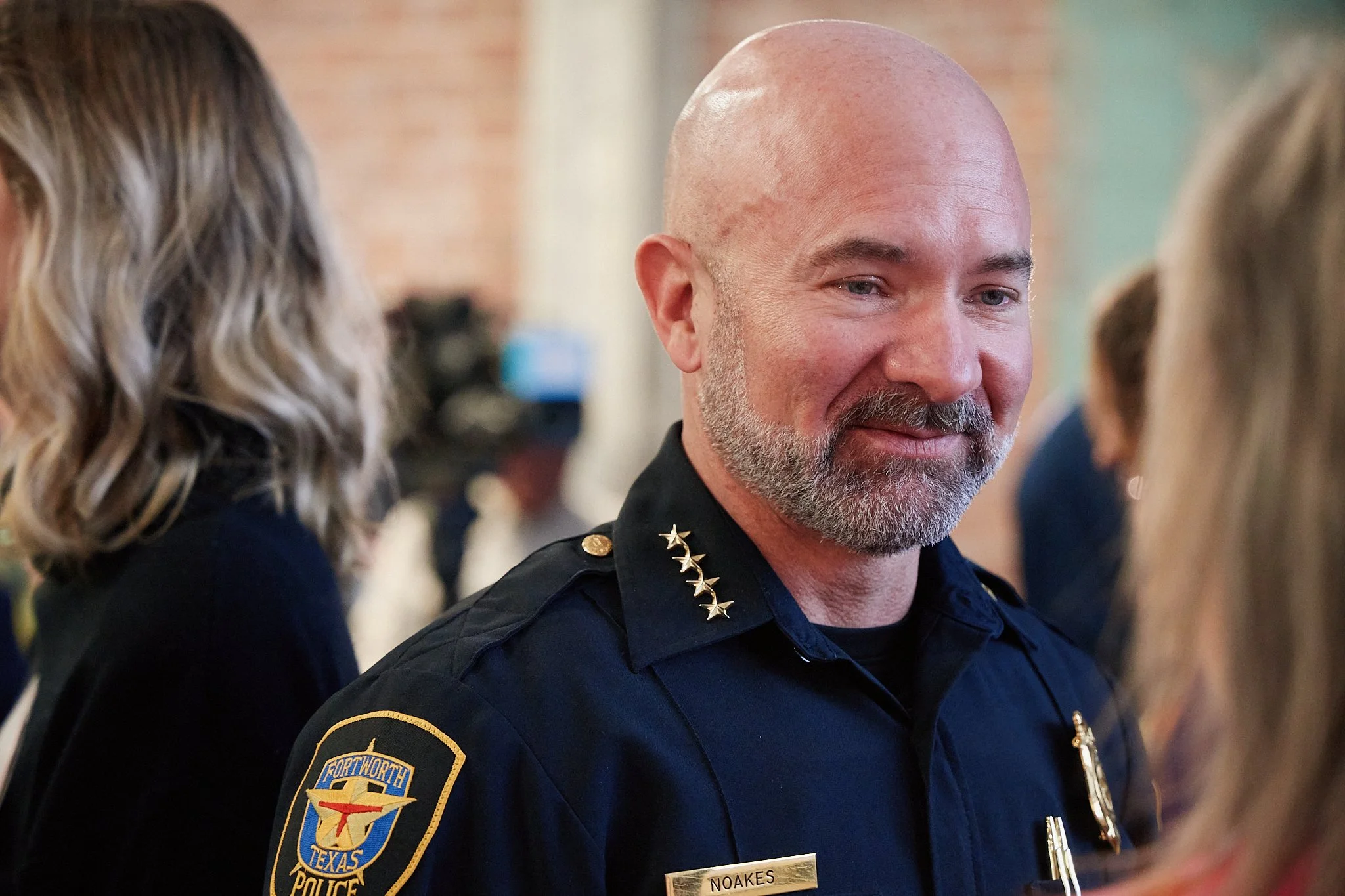 A smiling police officer in uniform with a patch that reads "Fort Worth Texas Police" speaking with a woman at an indoor event.