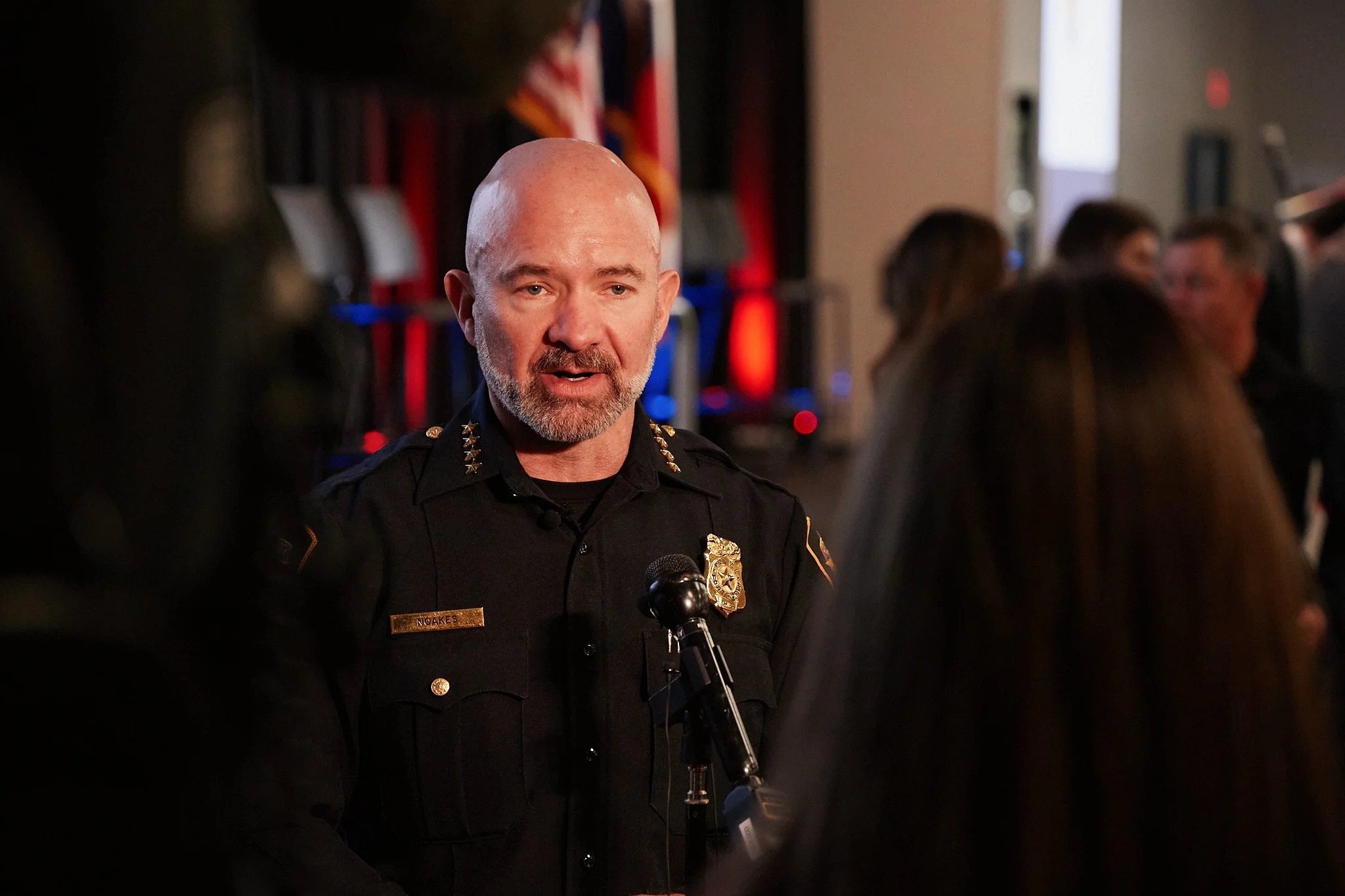 A police officer with a badge and uniform speaking to a group of people at an indoor event.