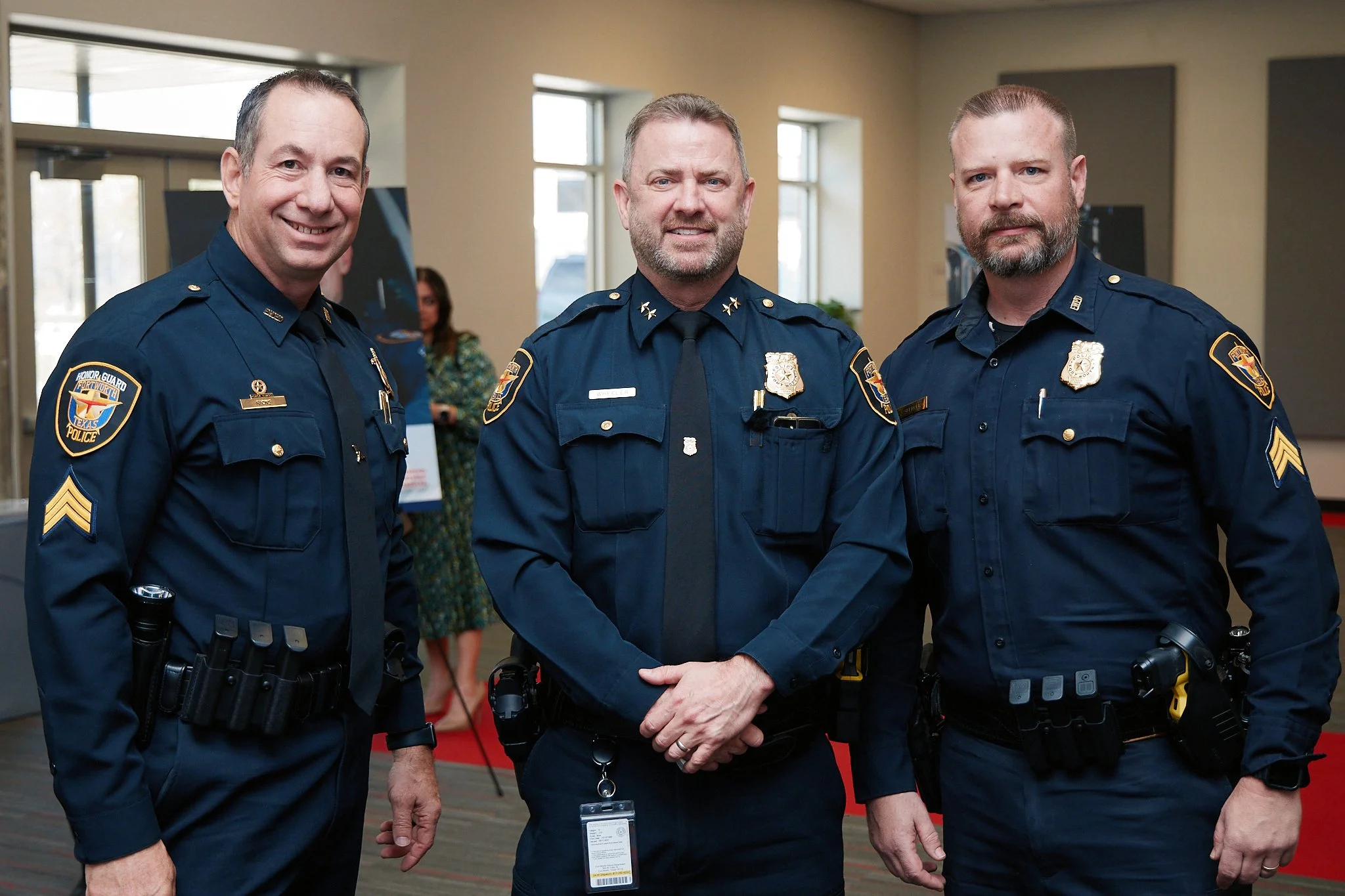 Three police officers in uniform standing together indoors, smiling at the camera.