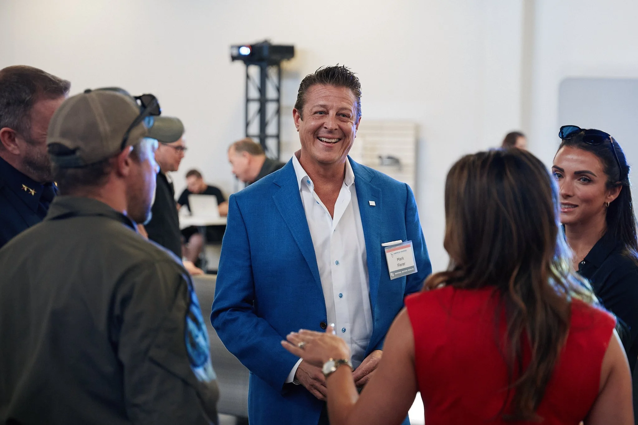 A man in a blue suit smiling and talking with three women at a social event or conference.