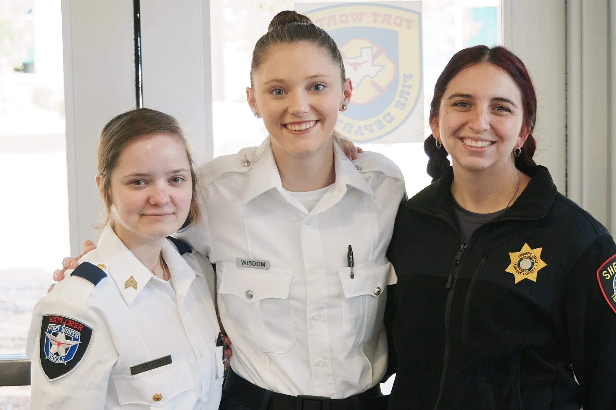 Three women in uniform standing together and smiling indoors.