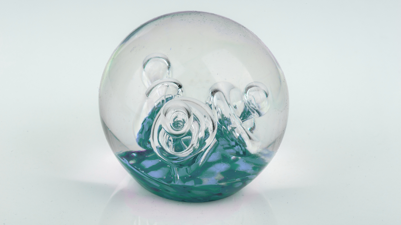 Clear glass paperweight with teal and blue swirls on a white background