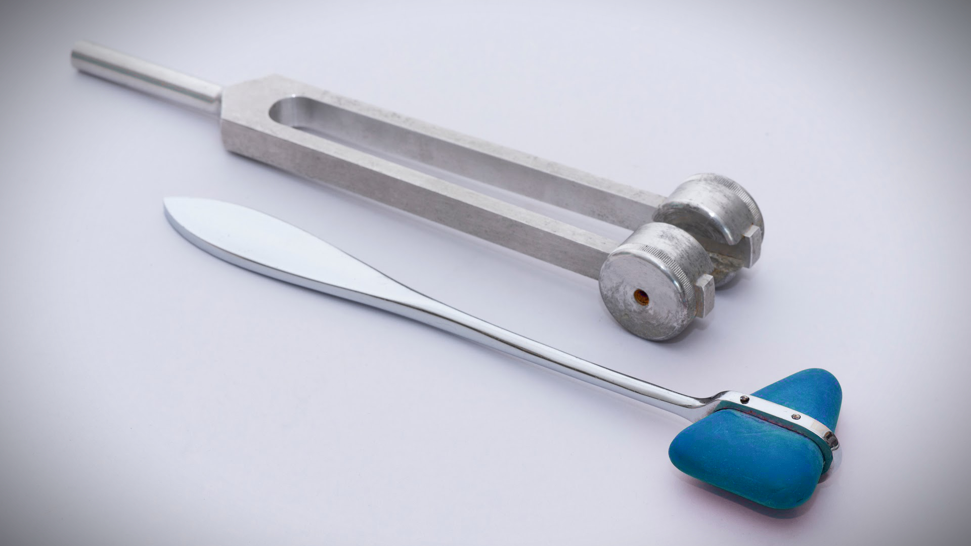 Tuning fork and small striking hammer on a light surface