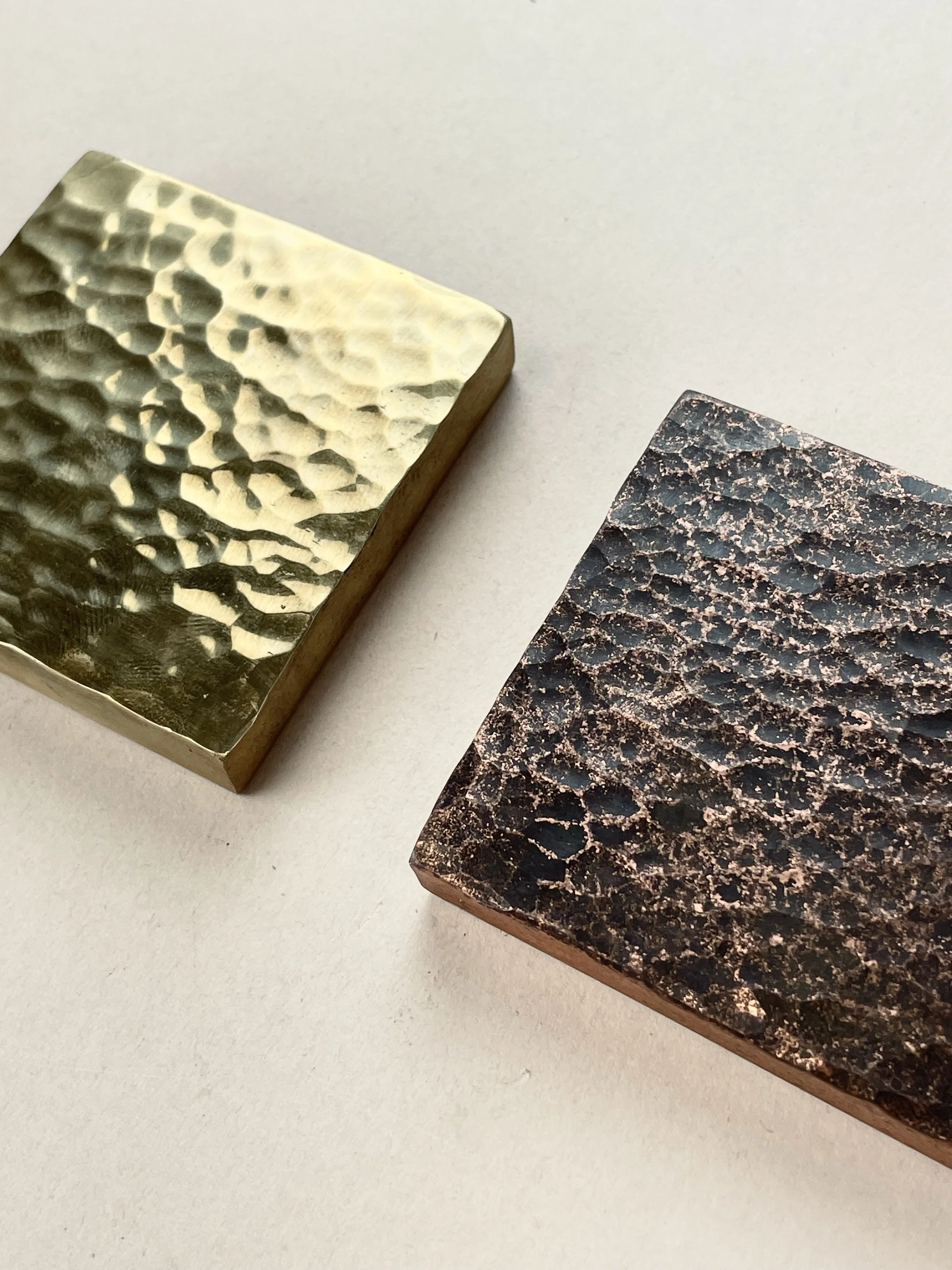 Close-up of two textured metallic blocks, one gold and one copper, on a white surface.
