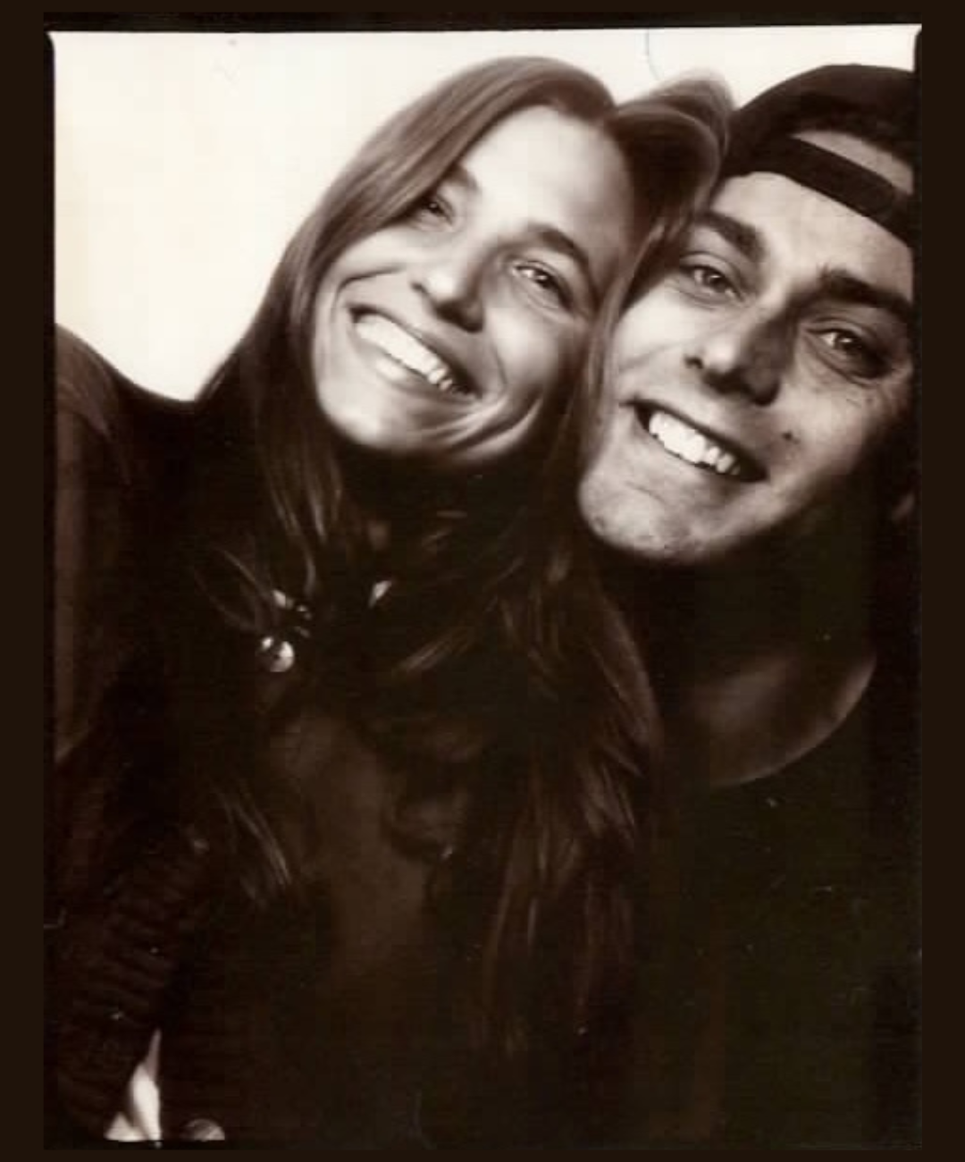 Black and white photo of a smiling woman and man, both with long hair, close together and looking at the camera.