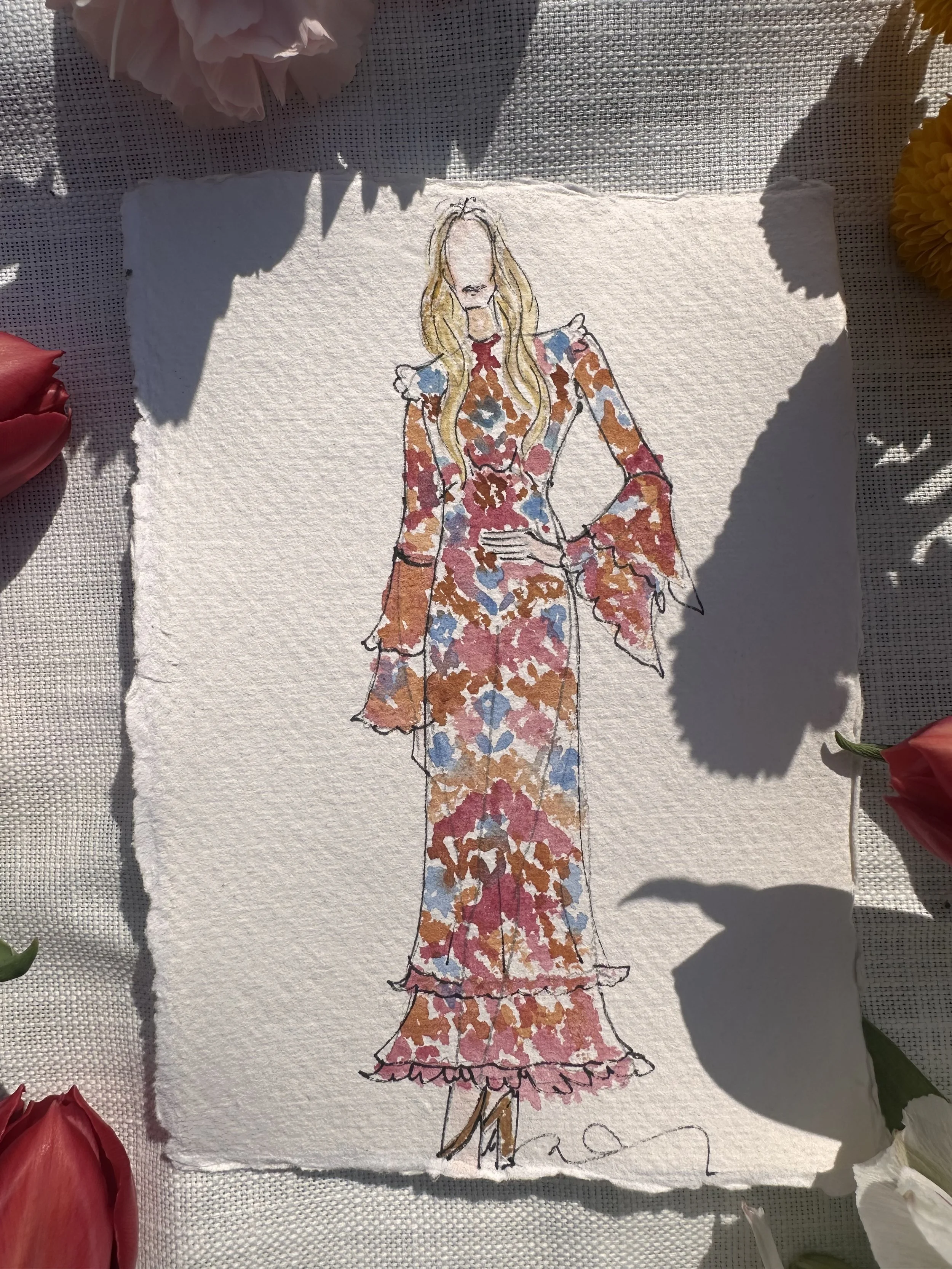 Hand-drawn fashion illustration of a woman in a long, colorful floral dress with ruffles and bell sleeves, with blurred background and surrounding flowers.