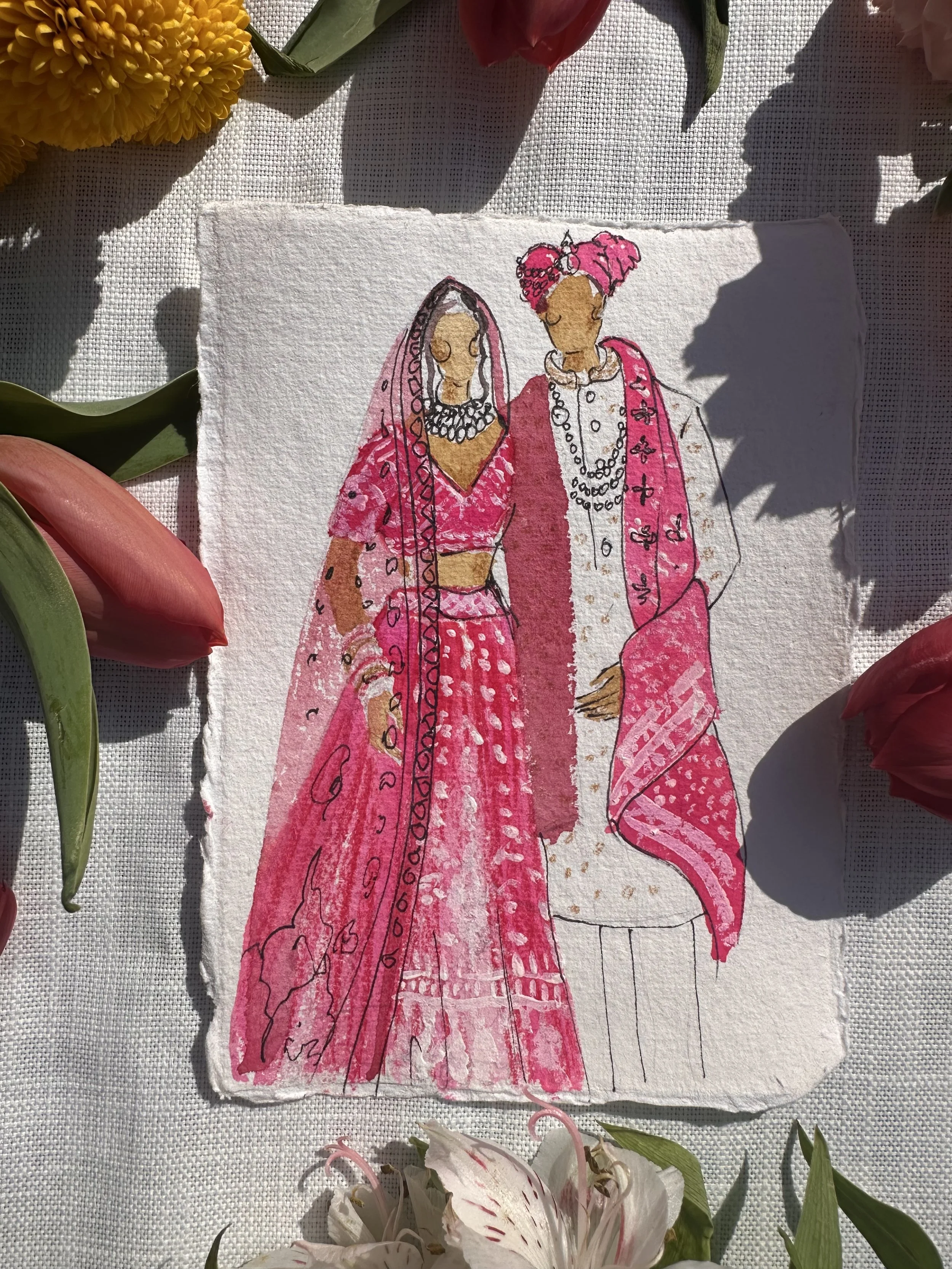 A watercolor illustration of two women dressed in traditional Indian attire, with one woman wearing a pink lehenga and the other wearing a pink saree with a white kurta, surrounded by flowers.